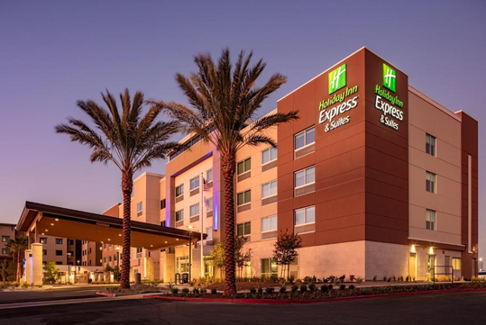 Holiday Inn Express & Suites building at dusk, featuring palm trees, warm lighting, and clear sky in the background.