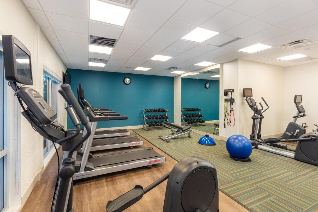 Modern gym with treadmills, stationary bikes, a set of dumbbells, kettlebells, medicine ball, and wall clock on blue accent wall.