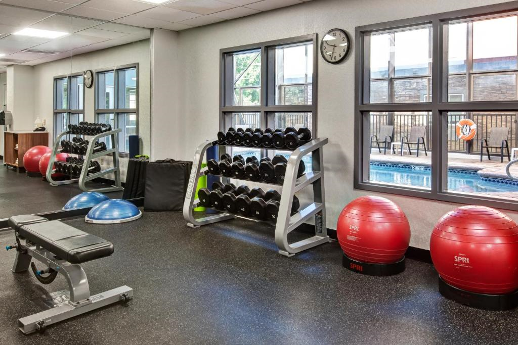 A gym with weights, a bench, exercise balls, and Bosu balls. Large windows overlook a pool area, with a clock showing 10:10.