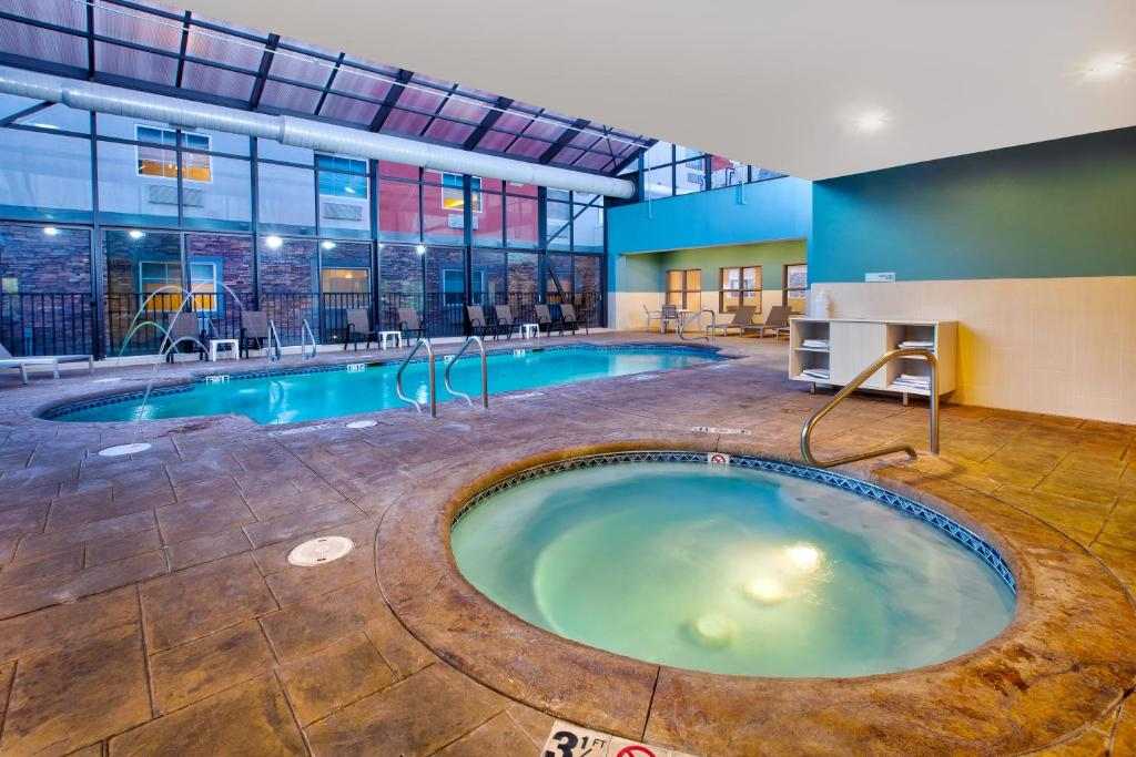 Indoor pool area with a jacuzzi in the foreground and a swimming pool in the background, surrounded by seating and large windows.