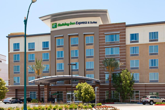 Front view of a Holiday Inn Express & Suites hotel with a modern facade, multiple windows, and palm trees in front.