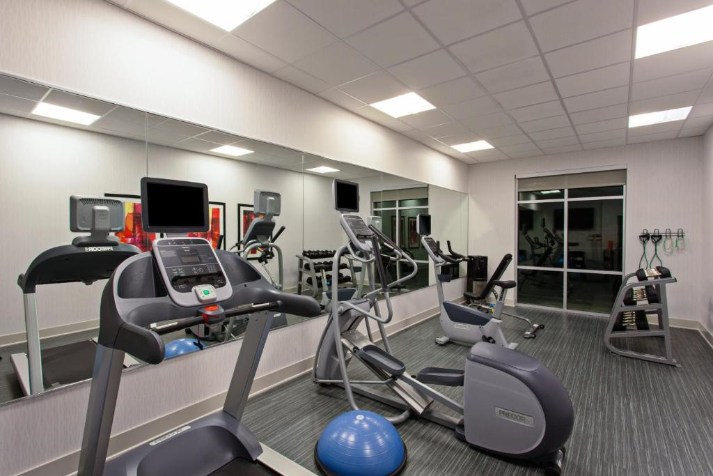 A modern gym features treadmills, elliptical machines, exercise balls, and free weights, with large mirrors on one wall and a window facing outside.