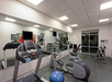 A modern gym features treadmills, elliptical machines, exercise balls, and free weights, with large mirrors on one wall and a window facing outside.