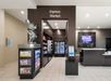 Hotel lobby with an "Express Market" featuring a statue of a mouse, snack shelves, and a fridge. Reception desk on the right with a digital screen behind it.