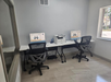 Small office space with two workstations featuring computers and a printer between them, on a white desk. Two ergonomic chairs are placed at each workstation, and a window is on the right.