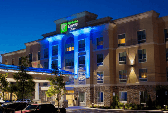 The front exterior of the Holiday Inn Express & Suites at night with blue lights illuminating the center.