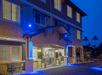 Hotel entrance illuminated with blue lights at night, featuring large windows, a covered walkway, and surrounding palm trees.