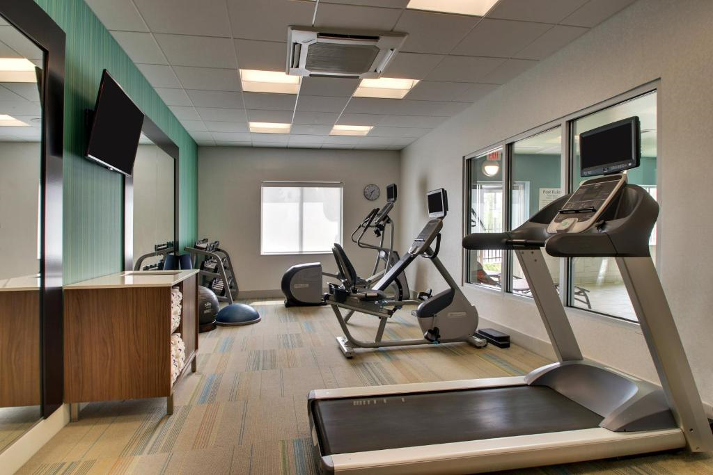 A gym room with a treadmill, elliptical, stationary bike, and exercise balls. Large windows and a wall-mounted TV are also visible.