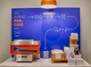 A pancake maker on a counter with condiments, plates, and utensils. A blue wall displays pancake-making instructions with icons and "Go ahead, pancake my day" text. An orange light hangs above.