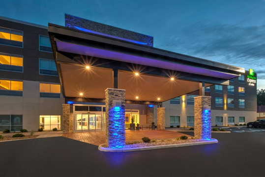 Modern hotel entrance with a lit canopy and illuminated stone pillars at dusk.
