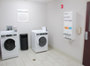 Laundry room with a washer, dryer, trash can, and a wall-mounted dispenser for soap, bleach, and softeners. A guest laundry sign is displayed above the machines.