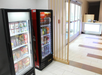 Vending machines stocked with snacks and drinks are positioned in a hallway near glass doors and a reception desk.