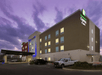 The exterior of the Holiday Inn Express & Suites New Braunfels with cars parking in the front and a purple sky overhead.