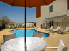 An outdoor swimming pool with bright blue water with lounge chairs and tables with umbrellas in the sides on a sunny day.