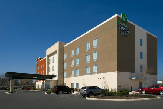 The exterior of the Holiday Inn Express & Suites New Braunfels with cars parking lot and a covered entrance on a sunny day.