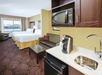 Hotel room with two beds, a couch, coffee table, and a kitchenette featuring a microwave, sink, mini-fridge, and coffee maker. A large window offers a view outside.