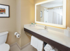 Bathroom with a large mirror, sink, and countertop. Towels are stored underneath, and toiletries are arranged on the counter. Shower with curtain is visible in the background.