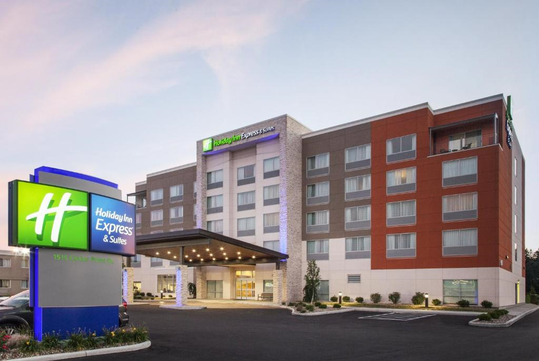 Exterior view of a Holiday Inn Express & Suites hotel with a modern design, featuring a well-lit entrance and a prominent sign in the foreground.