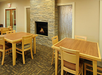 A room with wooden tables and chairs, a stone fireplace with a lit fire, and a textured glass partition.