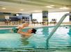 An adult holds a baby in the air while standing in an indoor swimming pool.