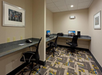 A small office space with two computer workstations, office chairs, a telephone, and framed artwork on beige walls.