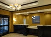 Hotel lobby with a front desk, a chandelier, and a sign on the wall. Walls are mustard-colored, and the floor is tiled. Doorway and windows are visible to the left.