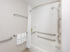 Bathroom with a white bathtub, grab bars, and a curved shower rod. White towels hang on a rack, and there are toiletries on a shelf.