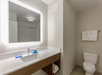 Modern bathroom with a large illuminated mirror, sink, toiletries, and a toilet. A towel is folded and placed on the towel rack.