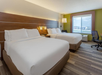 Hotel room with two double beds, a wooden headboard, white bedding, a window with a view, a desk and chair, and a green accent wall.
