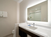 Modern bathroom with a large illuminated mirror above a white sink, a glass-enclosed shower, and neatly folded towels on a rack.