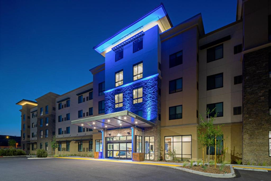 A modern hotel building at dusk with illuminated blue accents, large windows, and a covered entrance.