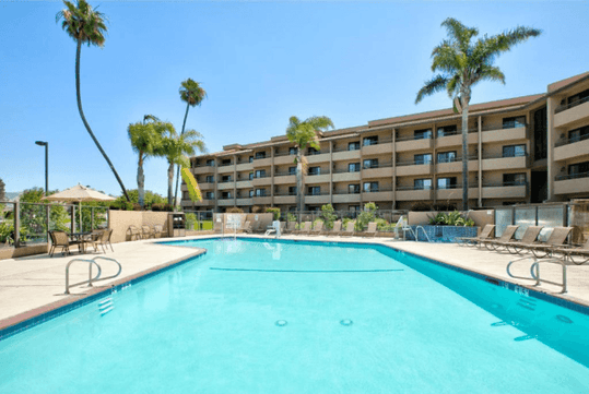 Outdoor pool surrounded by trees, private balconies, and sun loungers.