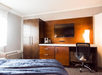 A bed, work area, closet, coffee maker, and a wall-mounted TV inside a guest room.