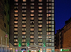 Night view of a tall Holiday Inn hotel building with illuminated windows, entrance canopy, and American flags at the front.
