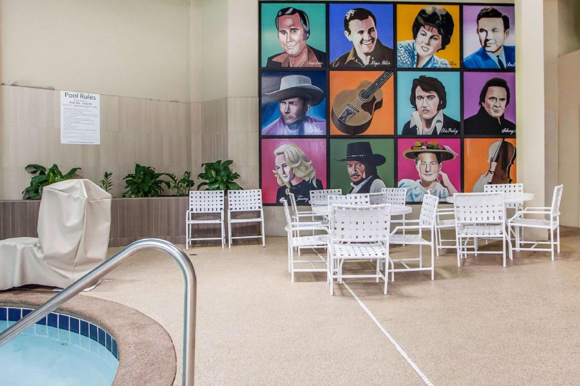 Indoor pool area with white chairs and tables in front of a wall featuring colorful portraits of various musicians. A hot tub is partially visible in the foreground.