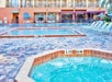 Outdoor pool and hot tub with lounge chairs and umbrellas.