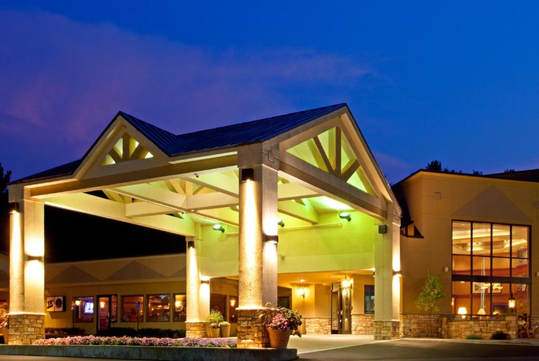The image shows a well-lit hotel entrance with a peaked roof and large support columns at dusk.