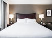 Hotel room with a large bed, flanked by two nightstands with geometric lamps. A floral artwork hangs on the wall.