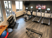 A small gym with treadmills, exercise bikes, a set of dumbbells, an exercise ball, a bench, and a wall-mounted TV.