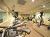 A well-lit gym with exercise equipment, including treadmills, stationary bikes, and weights, reflected in mirrors on the wall.