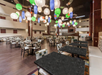 Spacious restaurant interior with multiple tables and chairs, colorful lamps hanging from the ceiling, and multi-level seating arrangements.