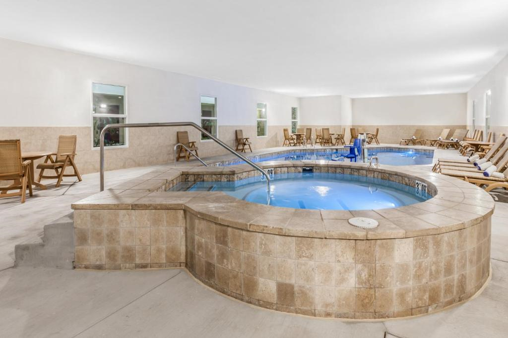 Indoor pool area with a circular hot tub surrounded by lounge chairs. The room has beige walls, large windows, and tiled flooring.