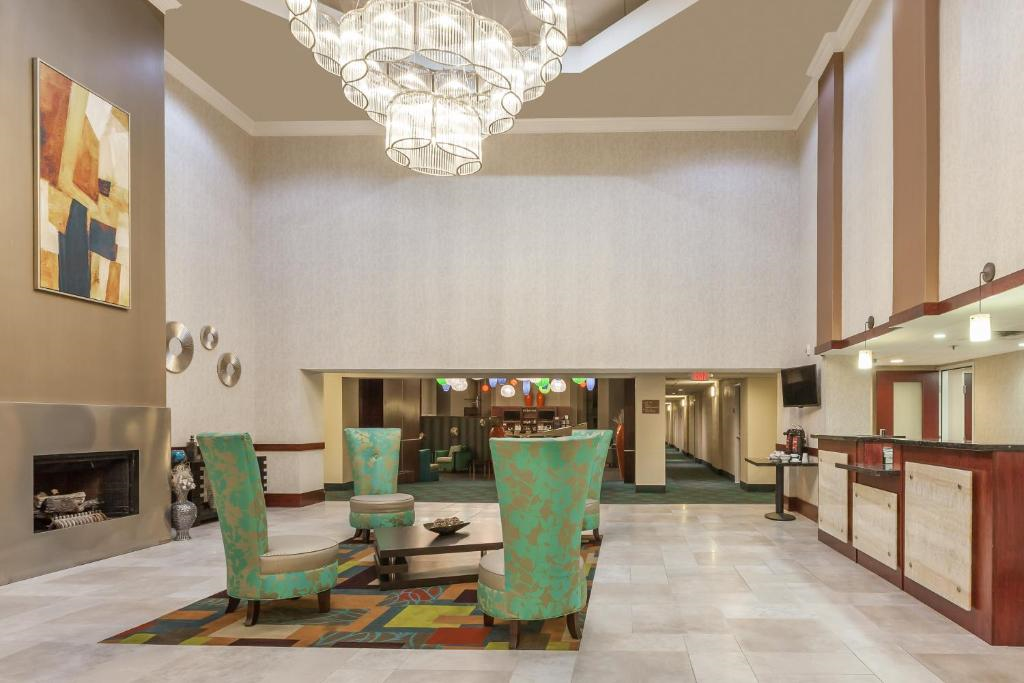 Hotel lobby with high ceiling, chandelier, teal patterned chairs around a low table, modern art on the wall, and a reception desk to the right.