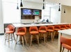 A bar with orange chairs lining it, two flat screen TV on the far wall, and windows letting in natural light at the Holiday Inn & Suites.