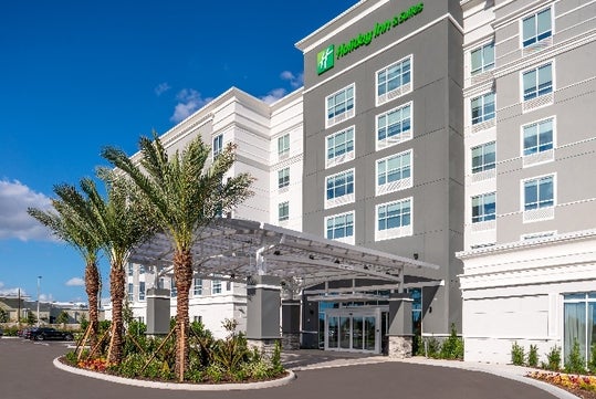 The front exterior and covered entrance of the Holiday Inn & Suites Orlando International Drive South with beautiful landscaping around the entrance.