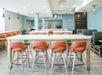 A dining room with several white hightop tables with orange chairs, gray booths, and a breakfast buffet at the Holiday Inn & Suites.