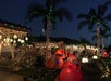 A house and palm trees are decorated with colorful Christmas lights and inflatable Santa figures at night.