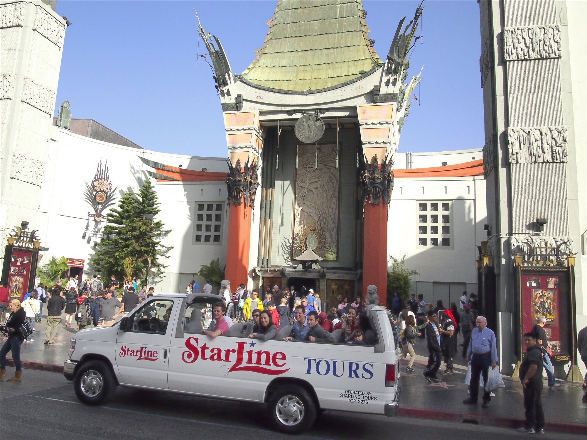 A StarLine Tours van with passengers stopped in front of Grauman's Chinese Theatre in Hollywood, with a crowd of people and the theater's iconic architecture in the background.