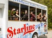 A group of people lean out of the windows of a Starline Tours bus, smiling and taking photos; “A Hollywood Tradition Since 1935” is written above.