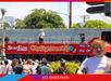 Ed Sheeran performs on the upper deck of a red CitySightseeing tour bus in front of a crowd, with a cameraman filming the event.